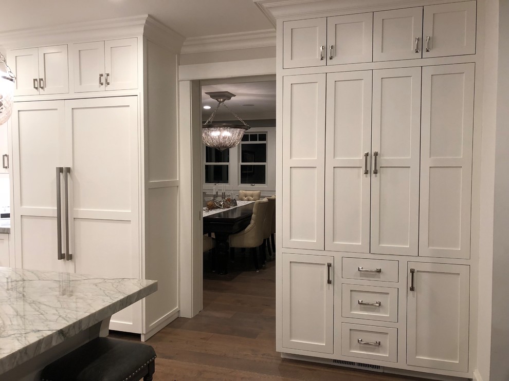 Photo of a large classic u-shaped kitchen pantry in San Francisco with a belfast sink, shaker cabinets, white cabinets, quartz worktops, white splashback, stone slab splashback, stainless steel appliances, dark hardwood flooring, an island and brown floors.