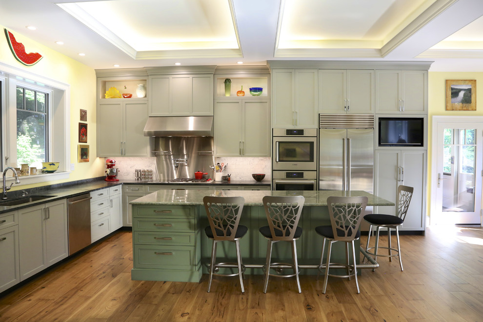 Exempel på ett mellanstort klassiskt grön grönt kök, med en undermonterad diskho, luckor med infälld panel, gröna skåp, granitbänkskiva, vitt stänkskydd, stänkskydd i marmor, rostfria vitvaror, ljust trägolv, en köksö och brunt golv