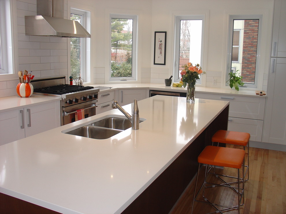 Mid-sized trendy l-shaped medium tone wood floor eat-in kitchen photo in Montreal with an undermount sink, shaker cabinets, white cabinets, white backsplash, subway tile backsplash, stainless steel appliances, solid surface countertops and an island