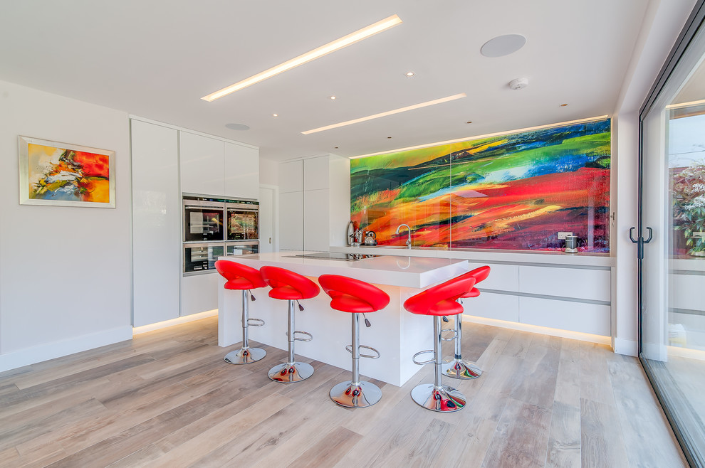 Inspiration for a medium sized contemporary kitchen/diner in Surrey with a submerged sink, flat-panel cabinets, white cabinets, quartz worktops, multi-coloured splashback, glass sheet splashback, stainless steel appliances, porcelain flooring and an island.