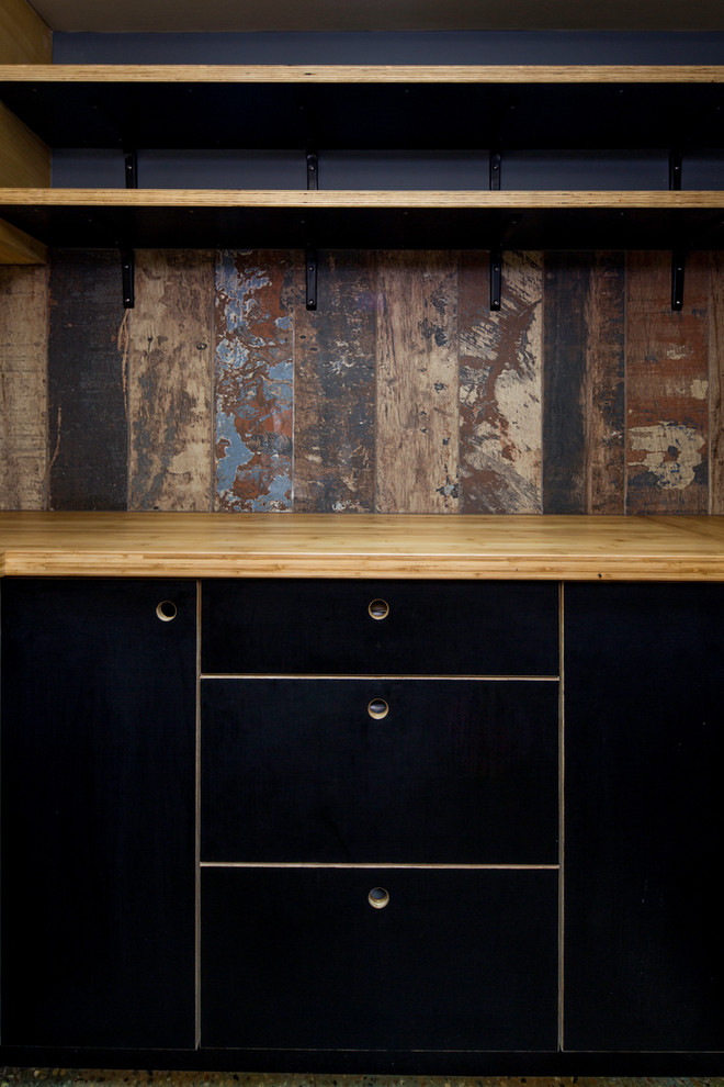 Immagine di una piccola cucina ad U industriale chiusa con lavello da incasso, ante lisce, ante nere, top in legno e pavimento in cemento