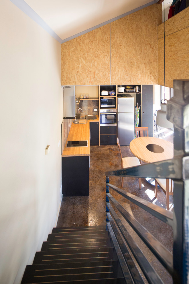 Foto de cocina industrial pequeña con fregadero encastrado, armarios con paneles lisos, puertas de armario negras, encimera de madera y suelo de cemento