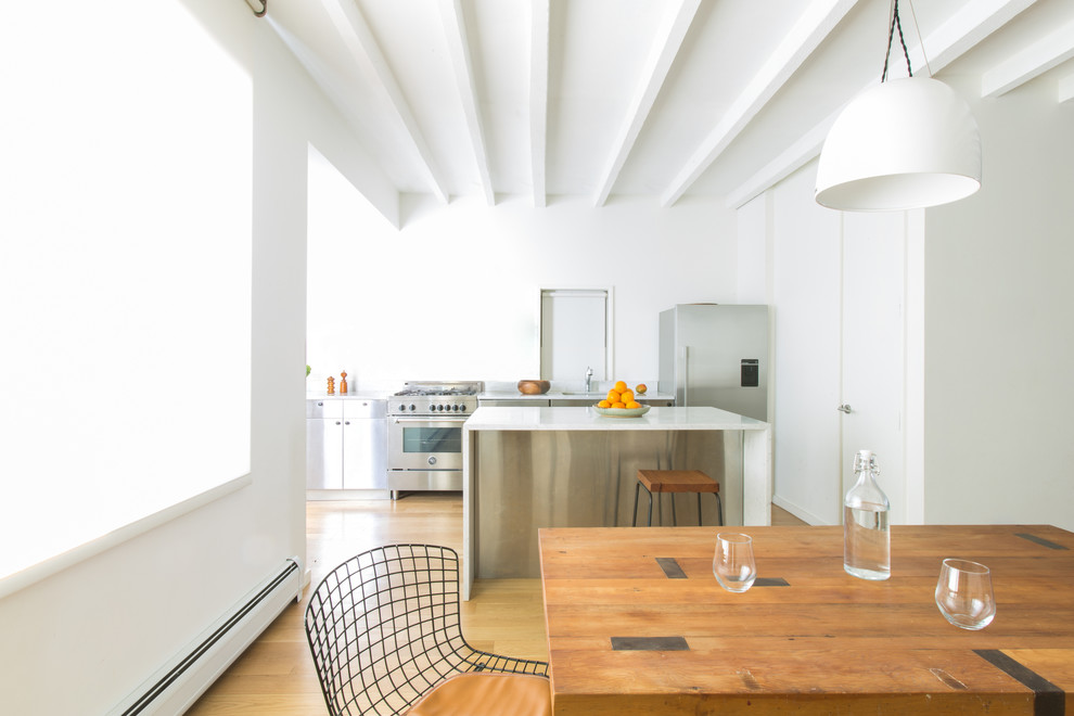Foto på ett funkis kök, med släta luckor, skåp i rostfritt stål, rostfria vitvaror, mellanmörkt trägolv och en köksö