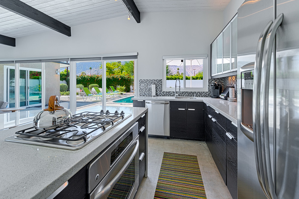 Exempel på ett 60 tals kök, med en undermonterad diskho, släta luckor, svart stänkskydd, stänkskydd i mosaik och rostfria vitvaror