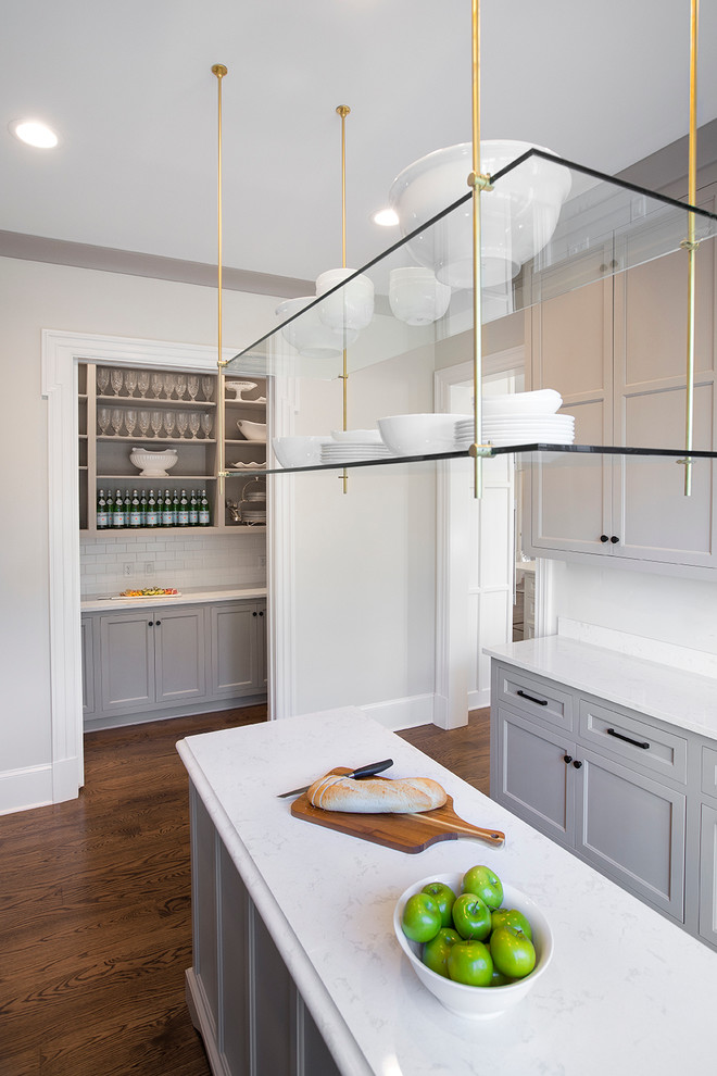 Inredning av ett klassiskt mellanstort u-kök, med marmorbänkskiva, vitt stänkskydd, stänkskydd i glaskakel, rostfria vitvaror, ljust trägolv, brunt golv, grå skåp, en köksö och luckor med infälld panel