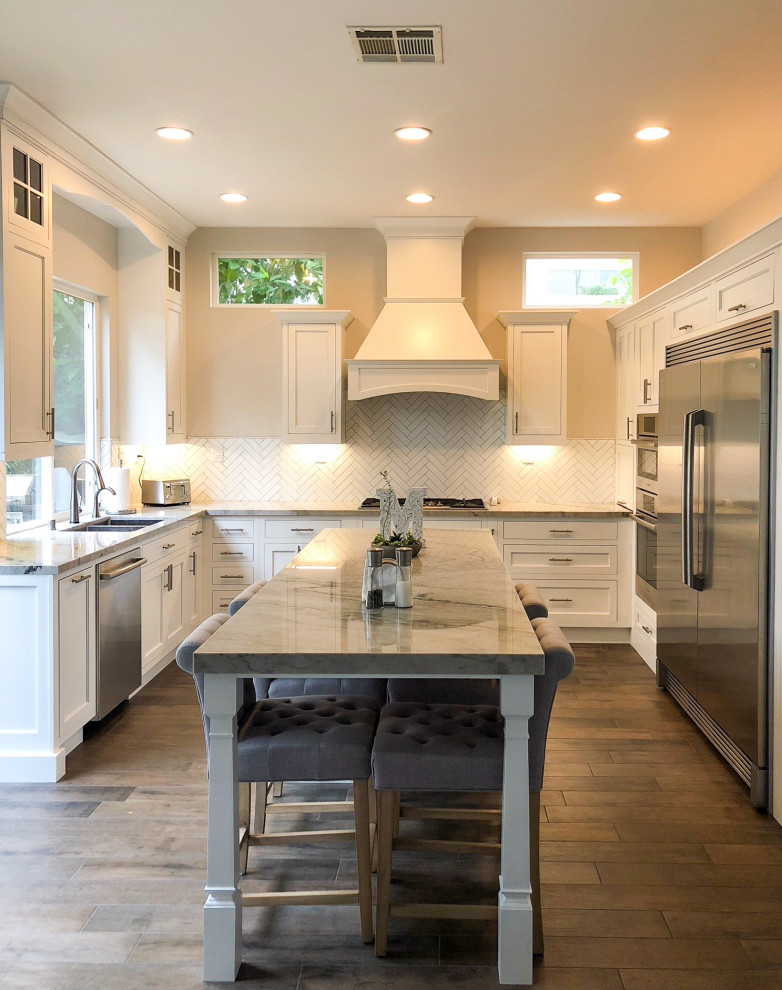 Inspiration for a medium sized traditional u-shaped kitchen/diner in San Diego with a submerged sink, shaker cabinets, white cabinets, white splashback, stainless steel appliances, medium hardwood flooring, an island and grey worktops.
