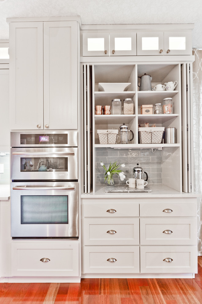 Klassisk inredning av ett mellanstort vit vitt kök, med en undermonterad diskho, skåp i shakerstil, grå skåp, bänkskiva i kvarts, blått stänkskydd, stänkskydd i keramik, rostfria vitvaror, mellanmörkt trägolv, en köksö och rött golv