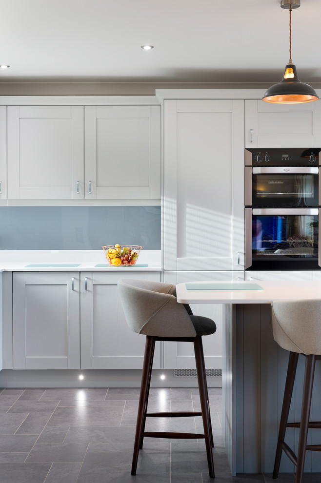 Example of a small minimalist l-shaped limestone floor and gray floor eat-in kitchen design in Cornwall with a drop-in sink, shaker cabinets, white cabinets, granite countertops, blue backsplash, glass tile backsplash, black appliances, an island and white countertops