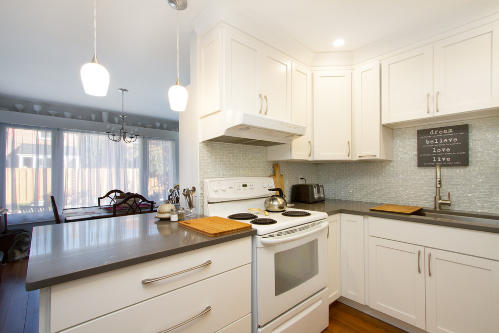 This is an example of a medium sized traditional u-shaped enclosed kitchen in Toronto with a submerged sink, shaker cabinets, white cabinets, engineered stone countertops, white splashback, mosaic tiled splashback, white appliances, laminate floors and a breakfast bar.