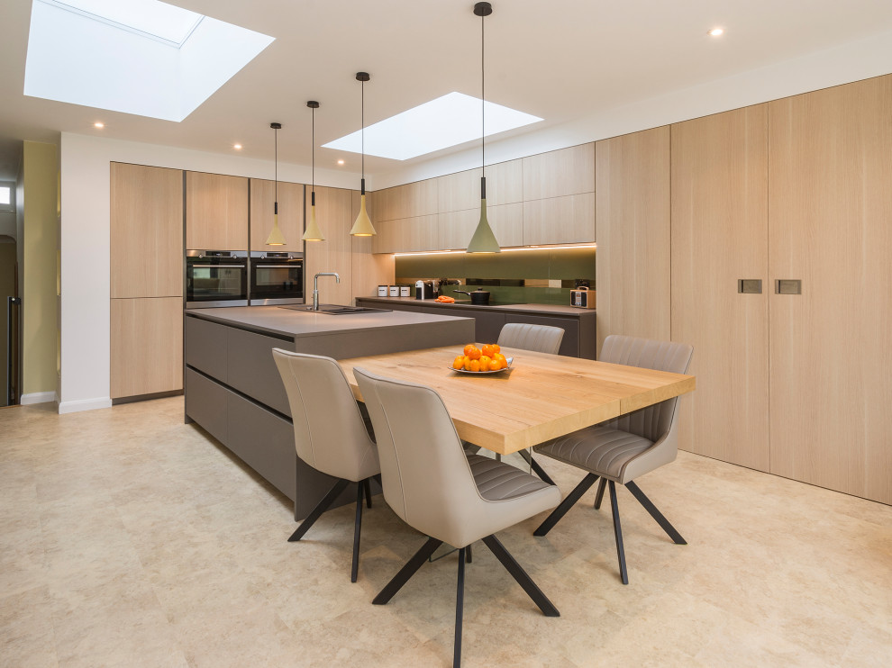 This is an example of a large contemporary l-shaped kitchen in Devon with a built-in sink, flat-panel cabinets, light wood cabinets, integrated appliances, porcelain flooring, an island, beige floors and grey worktops.