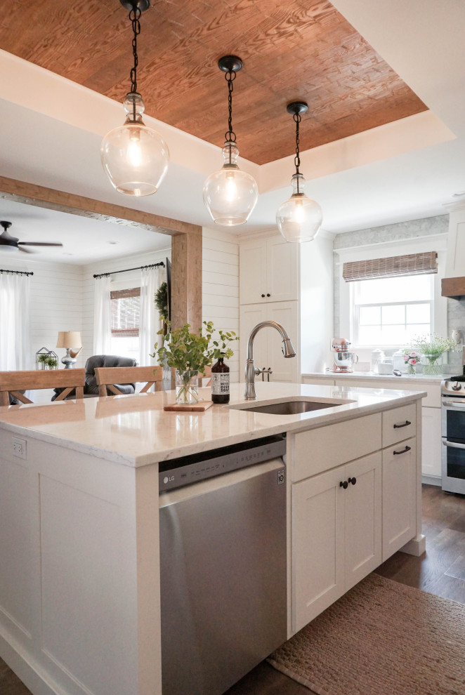 Foto på ett mellanstort lantligt vit kök, med en undermonterad diskho, skåp i shakerstil, vita skåp, bänkskiva i kvarts, grått stänkskydd, stänkskydd i marmor, rostfria vitvaror, mellanmörkt trägolv, en köksö och brunt golv