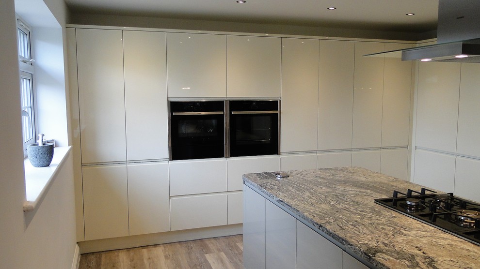 Modern inredning av ett stort kök, med en undermonterad diskho, släta luckor, beige skåp, granitbänkskiva, rostfria vitvaror, linoleumgolv, en köksö och brunt golv