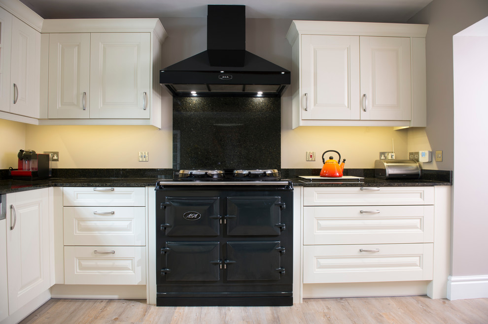 Foto de cocinas en L de estilo de casa de campo de tamaño medio con fregadero sobremueble, armarios con paneles con relieve, encimera de granito y electrodomésticos negros