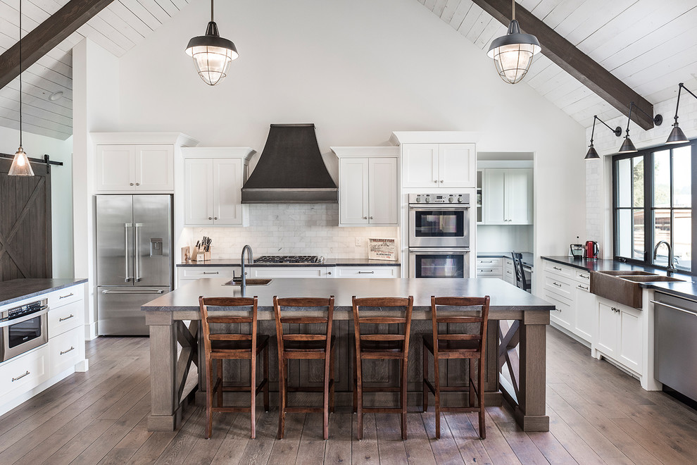 Inspiration for a cottage u-shaped medium tone wood floor and brown floor kitchen remodel in Vancouver with a farmhouse sink, shaker cabinets, white cabinets, white backsplash, stainless steel appliances, an island and black countertops
