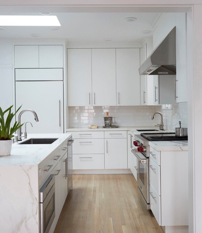 Exempel på ett mycket stort amerikanskt vit vitt kök, med en undermonterad diskho, släta luckor, vita skåp, bänkskiva i kvarts, vitt stänkskydd, stänkskydd i keramik, integrerade vitvaror, ljust trägolv, en köksö och brunt golv
