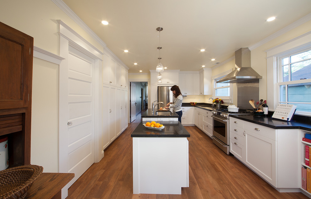 Inspiration for a mid-sized timeless l-shaped medium tone wood floor eat-in kitchen remodel in San Francisco with a single-bowl sink, shaker cabinets, white cabinets, laminate countertops, black backsplash, stainless steel appliances and an island