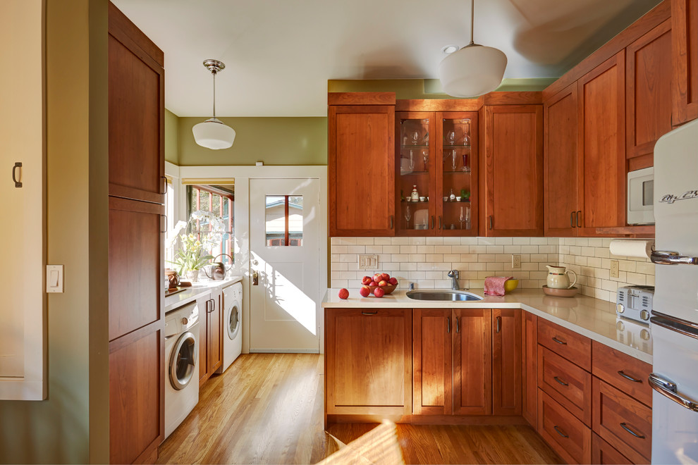 Imagen de cocinas en L de estilo americano de tamaño medio cerrada con fregadero bajoencimera, armarios estilo shaker, puertas de armario de madera oscura, encimera de cuarzo compacto, salpicadero blanco, salpicadero de azulejos de cerámica, electrodomésticos blancos y suelo de madera en tonos medios