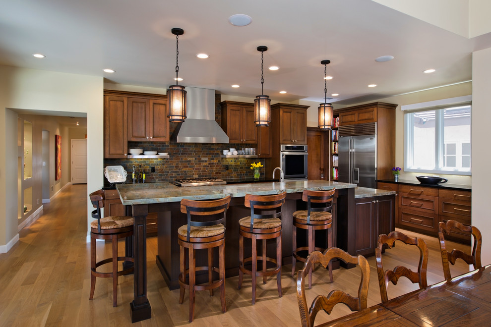 Foto de cocina tradicional renovada, de tamaño medio, con armarios con paneles con relieve, puertas de armario de madera en tonos medios, salpicadero marrón, electrodomésticos de acero inoxidable, suelo de madera clara, una isla, suelo beige y encimeras grises