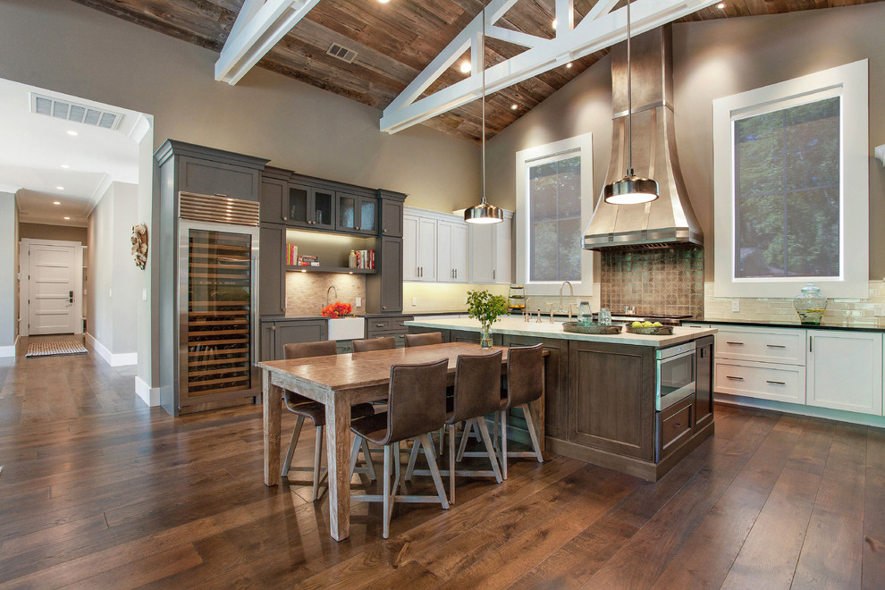 Inspiration for a large farmhouse u-shaped medium tone wood floor eat-in kitchen remodel in San Francisco with recessed-panel cabinets, white cabinets, soapstone countertops, gray backsplash, stainless steel appliances and an island