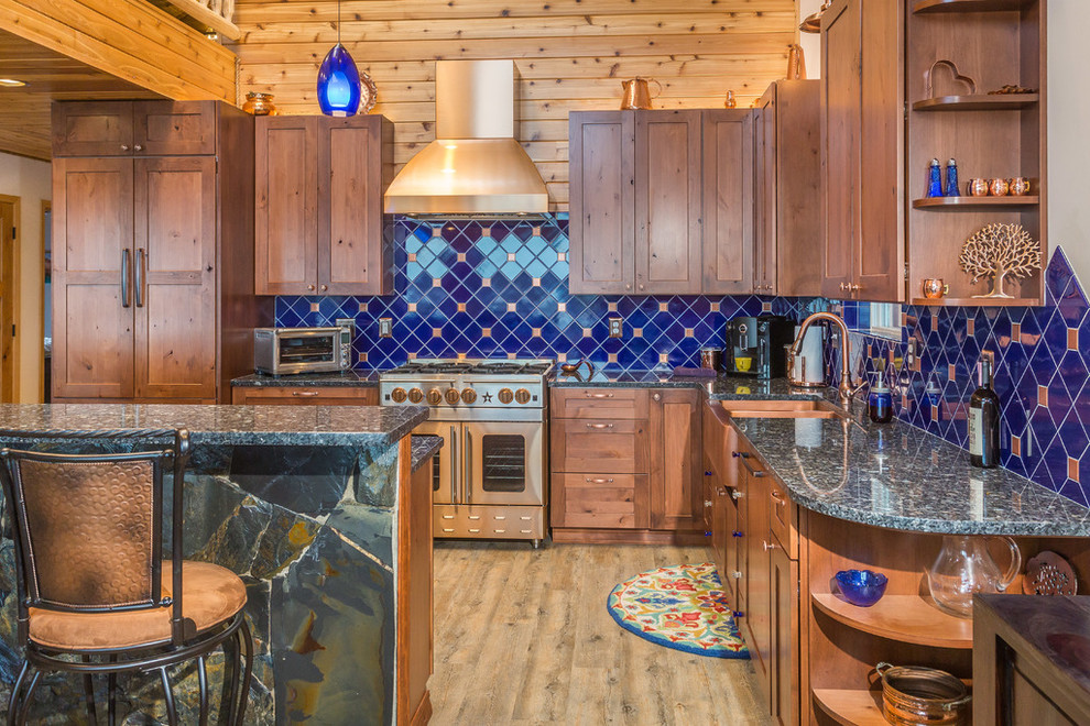 Foto på ett stort rustikt kök, med en rustik diskho, skåp i shakerstil, skåp i mellenmörkt trä, blått stänkskydd, rostfria vitvaror, en köksö, granitbänkskiva, stänkskydd i porslinskakel och ljust trägolv