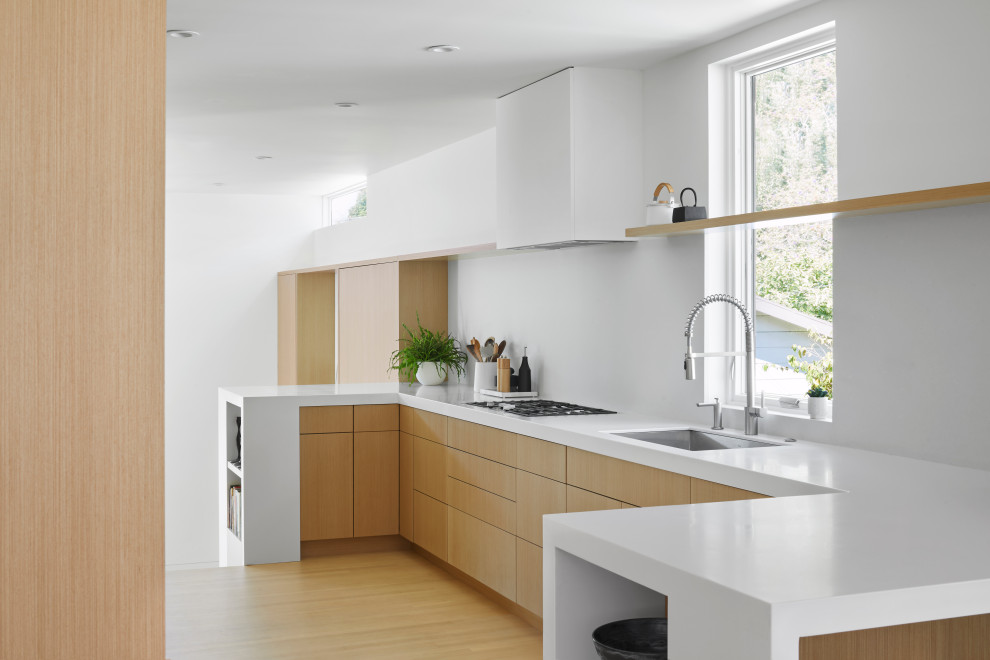 Design ideas for a modern u-shaped kitchen in San Francisco with a submerged sink, flat-panel cabinets, medium wood cabinets, medium hardwood flooring, a breakfast bar, brown floors and white worktops.
