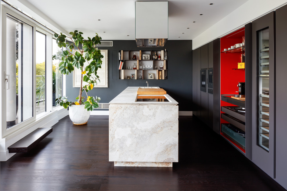 Große Moderne Küche mit flächenbündigen Schrankfronten, Kalkstein-Arbeitsplatte, dunklem Holzboden, Kücheninsel, grauen Schränken und Elektrogeräten mit Frontblende in London