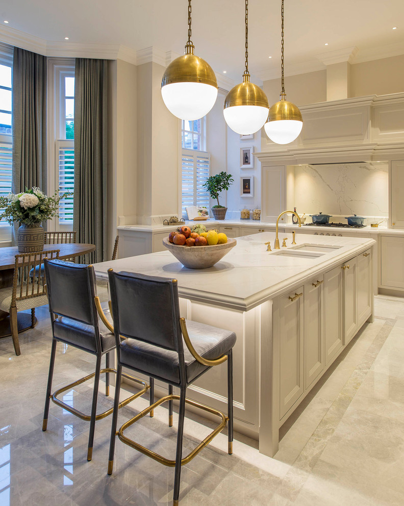 Example of a transitional l-shaped beige floor eat-in kitchen design in London with a double-bowl sink, recessed-panel cabinets, white backsplash, an island, white countertops, white cabinets and paneled appliances