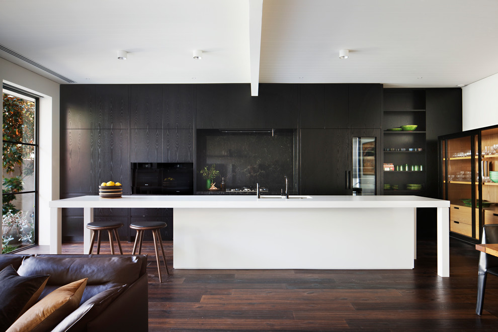 Пример оригинального дизайна: кухня-гостиная в стиле модернизм с двойной мойкой, плоскими фасадами, черным фартуком, техникой под мебельный фасад, темным паркетным полом, островом, коричневым полом и черно-белыми фасадами