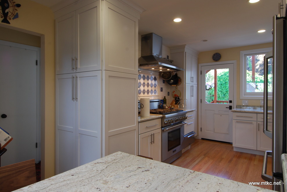 Bild på ett vintage kök, med luckor med infälld panel, vita skåp, granitbänkskiva, vitt stänkskydd, rostfria vitvaror, ljust trägolv, en halv köksö och gult golv