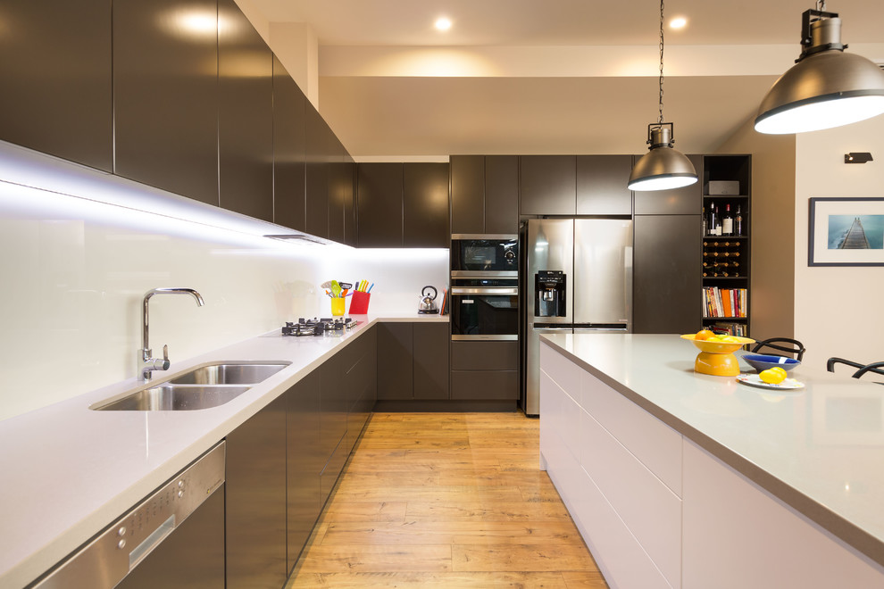 Moderne Küche in L-Form mit Unterbauwaschbecken, flächenbündigen Schrankfronten, grauen Schränken, Küchengeräten aus Edelstahl, braunem Holzboden, Kücheninsel, braunem Boden und weißer Arbeitsplatte in Sonstige