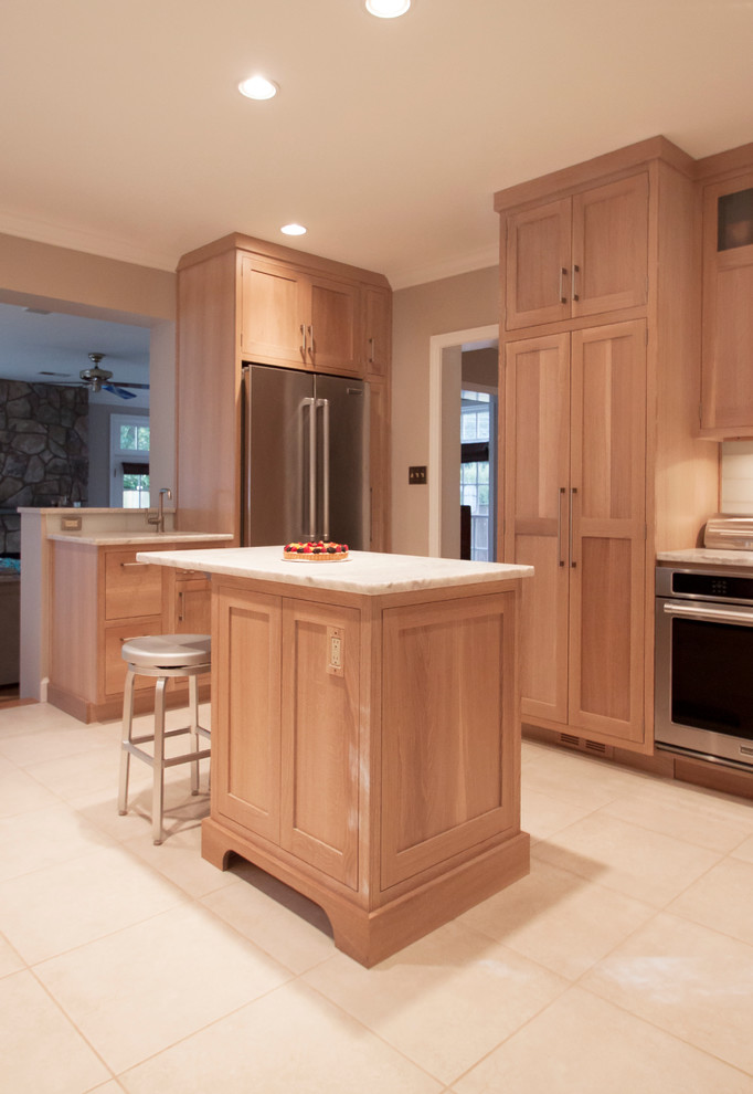 Cette photo montre une cuisine américaine chic en bois clair avec un placard à porte shaker, un plan de travail en quartz, une crédence blanche, une crédence en carreau de verre et un électroménager en acier inoxydable.