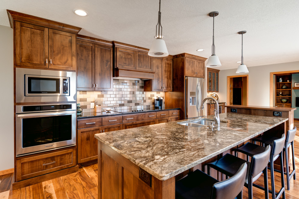 Example of a mid-sized transitional single-wall medium tone wood floor and brown floor eat-in kitchen design in Minneapolis with a double-bowl sink, shaker cabinets, medium tone wood cabinets, granite countertops, multicolored backsplash, stainless steel appliances, an island and subway tile backsplash