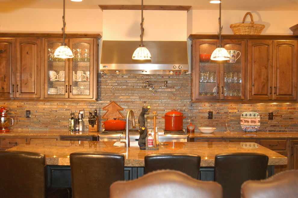 This is an example of a large rustic l-shaped kitchen/diner in Denver with raised-panel cabinets, dark wood cabinets, granite worktops, multi-coloured splashback, stone tiled splashback, stainless steel appliances, an island and brown worktops.