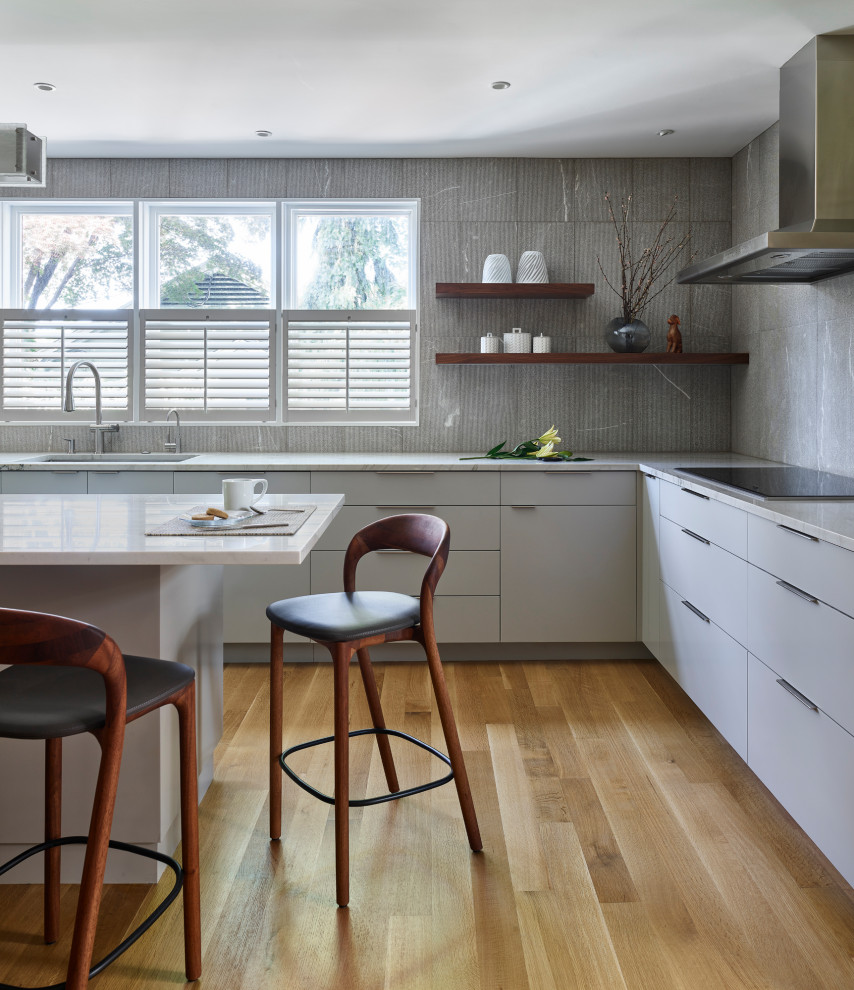 Design ideas for a medium sized traditional l-shaped kitchen/diner in Boston with an integrated sink, flat-panel cabinets, white cabinets, quartz worktops, grey splashback, stone tiled splashback, stainless steel appliances, medium hardwood flooring, an island and multicoloured worktops.