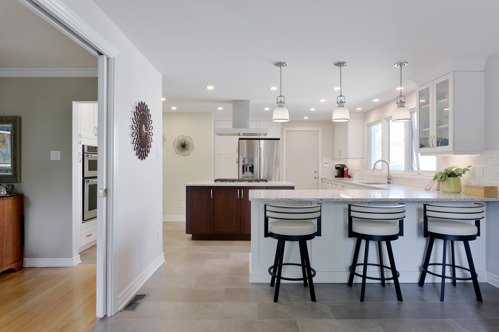 Inspiration for a large traditional u-shaped open plan kitchen in Ottawa with a submerged sink, shaker cabinets, white cabinets, engineered stone countertops, white splashback, metro tiled splashback, stainless steel appliances, porcelain flooring, an island, beige floors and grey worktops.
