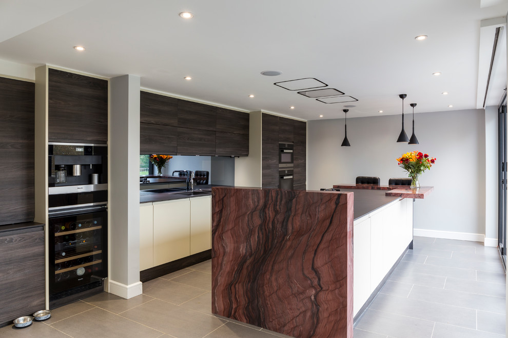 Moderne Küche mit Unterbauwaschbecken, flächenbündigen Schrankfronten, dunklen Holzschränken, schwarzen Elektrogeräten und Kücheninsel in London