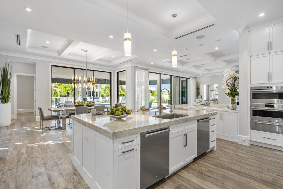 Foto på ett funkis vit kök, med en undermonterad diskho, skåp i shakerstil, vita skåp, marmorbänkskiva, beige stänkskydd, stänkskydd i marmor, rostfria vitvaror, mellanmörkt trägolv, en köksö och brunt golv