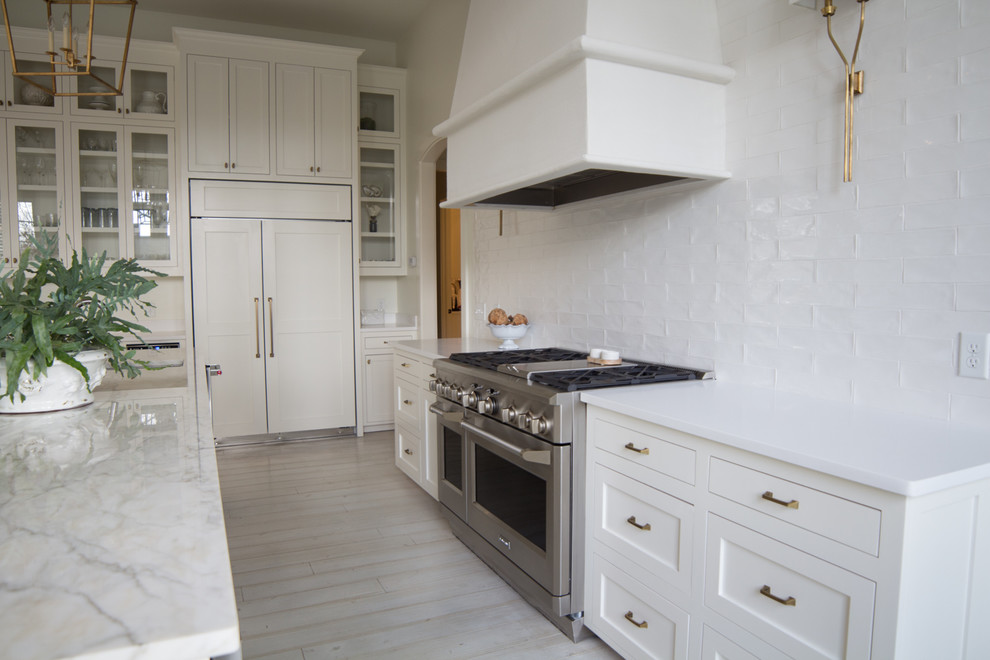 Ejemplo de cocina comedor rústica con puertas de armario blancas, salpicadero blanco, electrodomésticos de acero inoxidable y una isla