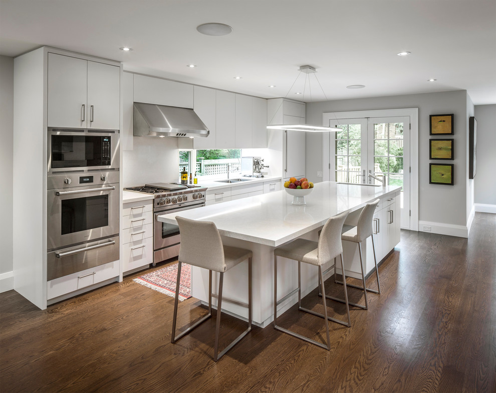 This is an example of a large classic single-wall open plan kitchen in Toronto with a double-bowl sink, flat-panel cabinets, white cabinets, engineered stone countertops, white splashback, window splashback, stainless steel appliances, dark hardwood flooring, an island and brown floors.