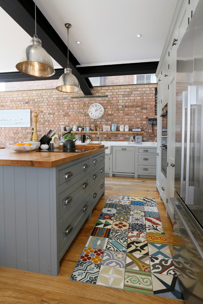 Design ideas for a rustic l-shaped open plan kitchen in London with a belfast sink, shaker cabinets, grey cabinets, wood worktops, stainless steel appliances, light hardwood flooring and an island.