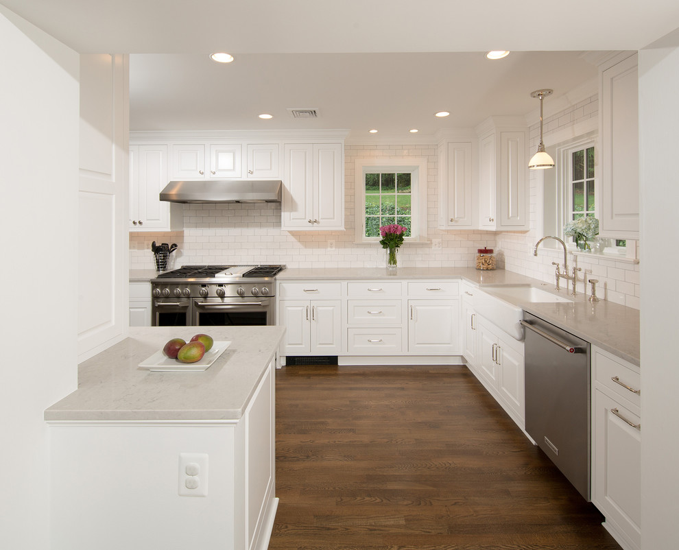 Inspiration for a mid-sized timeless u-shaped medium tone wood floor and brown floor enclosed kitchen remodel in DC Metro with a farmhouse sink, raised-panel cabinets, white cabinets, quartz countertops, gray backsplash, subway tile backsplash, stainless steel appliances and a peninsula