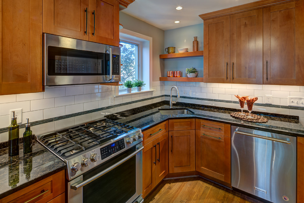 This is an example of a medium sized classic u-shaped kitchen/diner in DC Metro with a submerged sink, shaker cabinets, medium wood cabinets, engineered stone countertops, white splashback, porcelain splashback, stainless steel appliances, light hardwood flooring, a breakfast bar, brown floors and black worktops.