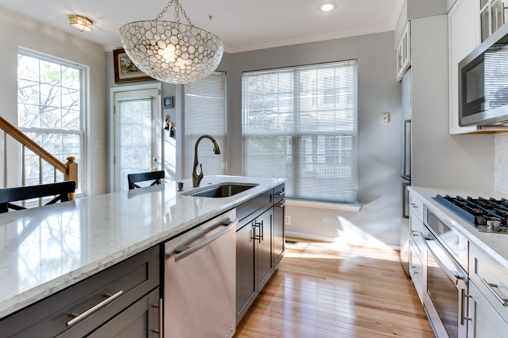 Example of a small transitional galley medium tone wood floor kitchen design in DC Metro with an undermount sink, shaker cabinets, white cabinets, quartz countertops, stainless steel appliances and an island