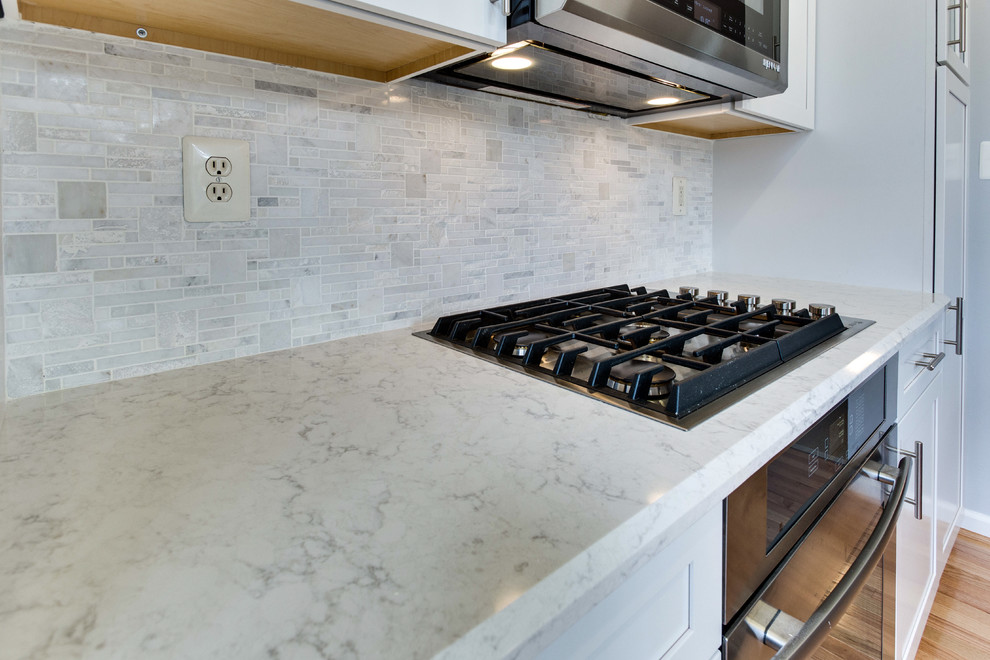 Example of a small transitional galley medium tone wood floor kitchen design in DC Metro with an undermount sink, shaker cabinets, white cabinets, quartz countertops, stainless steel appliances and an island