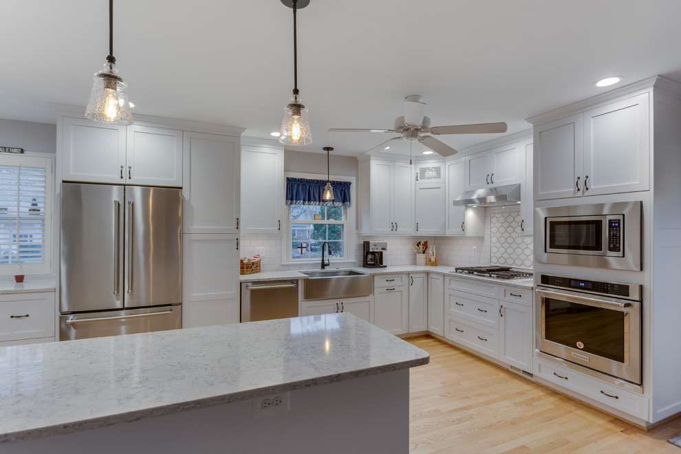 Design ideas for a classic kitchen in DC Metro with a belfast sink, recessed-panel cabinets, white cabinets, engineered stone countertops, white splashback, metro tiled splashback, stainless steel appliances, light hardwood flooring, an island and grey worktops.