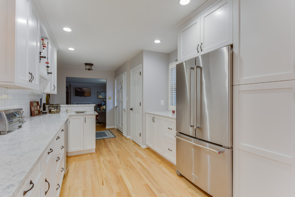 Bild på ett vintage grå grått kök, med en rustik diskho, luckor med infälld panel, vita skåp, bänkskiva i kvarts, vitt stänkskydd, stänkskydd i tunnelbanekakel, rostfria vitvaror, ljust trägolv och en köksö