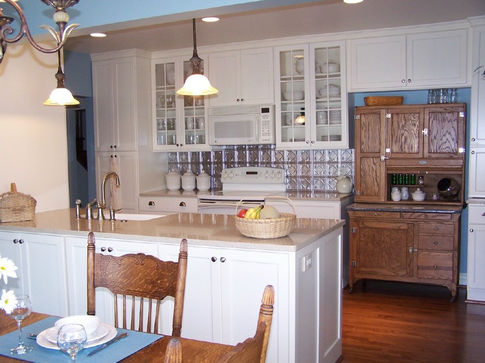 Klassisk inredning av ett kök, med en rustik diskho, släta luckor, vita skåp, bänkskiva i kvarts, stänkskydd med metallisk yta, stänkskydd i metallkakel och vita vitvaror