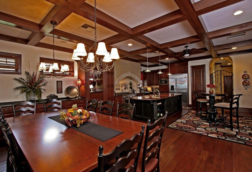 Large tuscan l-shaped dark wood floor and brown floor eat-in kitchen photo in Jacksonville with raised-panel cabinets, dark wood cabinets, granite countertops, beige backsplash, stone tile backsplash, stainless steel appliances and an island