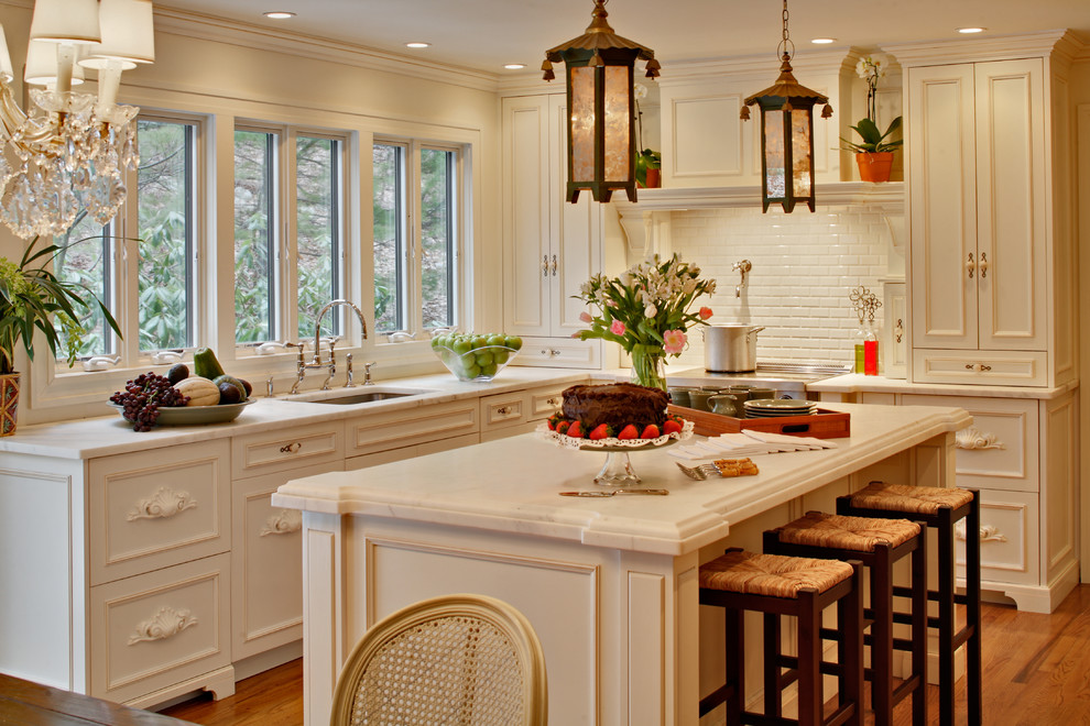 Foto på ett kök, med luckor med infälld panel, rostfria vitvaror, stänkskydd i tunnelbanekakel, en undermonterad diskho, vita skåp, marmorbänkskiva och vitt stänkskydd