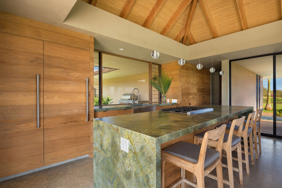 Küche mit Landhausspüle, hellbraunen Holzschränken, Granit-Arbeitsplatte, Elektrogeräten mit Frontblende, Kalkstein, Kücheninsel und grauem Boden in Hawaii